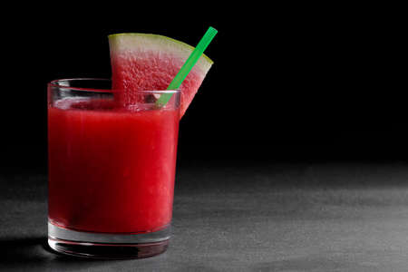 Watermelon smoothies in a glass with a slice of watermelon on a black background with a place for writingの写真素材
