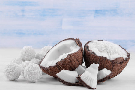 Halves of coconut with coconut shavings and small pieces of coconut on a white wooden background.