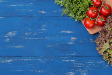 fresh greens and tomatoes on a cutting board. ingredients for cooking. On a blue wooden table with a place for inscriptionの写真素材