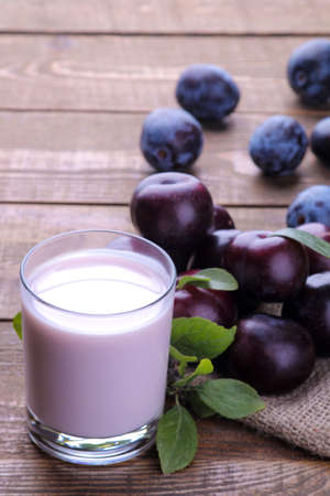 yoghurt from a plum in a glass with mature fresh plums in the background on a brown wooden tableの写真素材