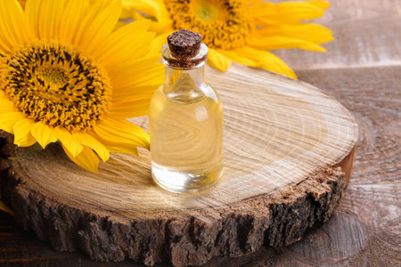 Composition with sunflower oil and sunflower flowers on a wooden stand on a brown wooden tableの写真素材