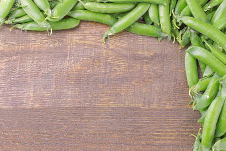green fresh peas in trimmings lined with a frame on a brown wooden table with a place for the inscription. top viewの写真素材