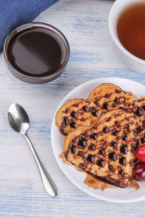 Delicious sweet Belgian waffles in the form of hearts with chocolate and berries on a blue wooden background. breakfastの写真素材