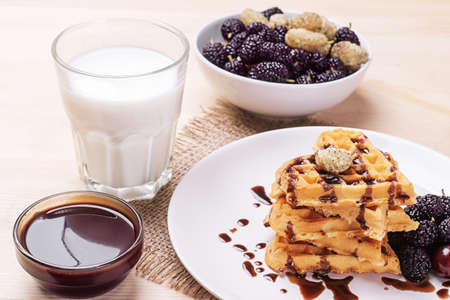 Delicious sweet Belgian waffles in the form of hearts with chocolate and berries with a glass of milk. breakfast. on a natural wooden backgroundの写真素材