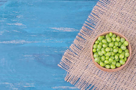 green fresh peas in a wooden bowl on a blue wooden table with a place for writing. top viewの写真素材