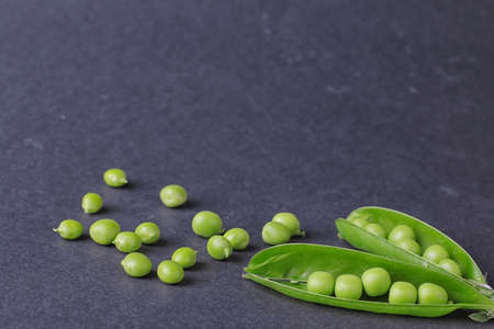 green fresh peas in a trimmings on a black background with a place for an inscriptionの写真素材