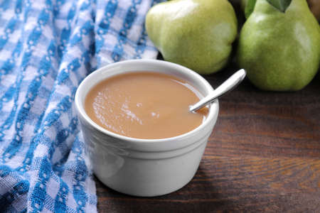Pear puree in a white bowl next to fresh ripe pears on a wooden brown tableの写真素材