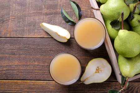 Pear juice in a glass with fresh ripe pears on a brown wooden table. top viewの写真素材