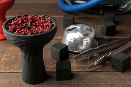 silicone bowl for hookah with tobacco and various accessories for making hookah. coals, tongs, kolaud on a brown wooden table. close-up. accessories for hookah.の写真素材