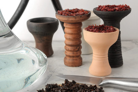 Transparent hookah with a black mouthpiece and a clay bowl with tobacco and various accessories for...