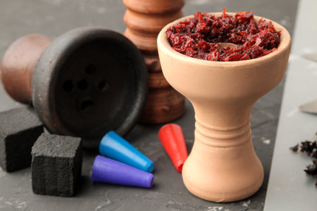 clay bowl for hookah with tobacco and various accessories for making hookah. coals, tongs, kolaud against a dark background. close-up. accessories for hookah.の写真素材