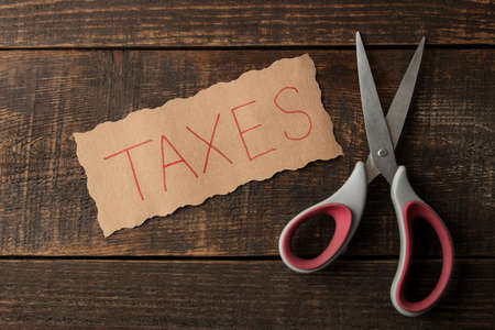 The word taxes with scissors on a brown wooden background. view from aboveの写真素材
