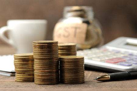 The word GST in the background and a stack of coins with a calculator pen and coffee on a brown...