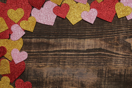 Multicolored shiny hearts on a brown wooden background. frame of hearts, top view with space for textの写真素材