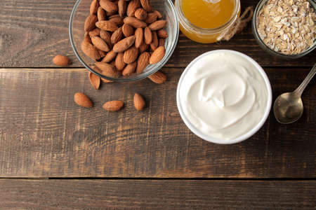 Greek yogurt in a ceramic bowl with almonds and honey, oatmeal next to a spoon on a brown wooden background. healthy food. natural yoghurt. breakfast. top view with space for textの写真素材