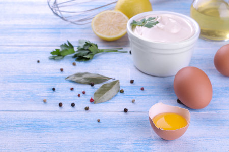 Mayonnaise in a white bowl and ingredients for making mayonnaise on a blue wooden background. white sauce.の写真素材