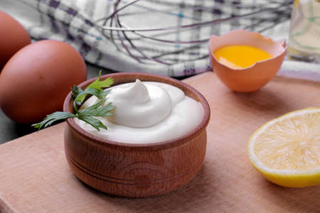 Mayonnaise in a wooden bowl and ingredients for making mayonnaise on a cutting board. white sauce. close-upの写真素材