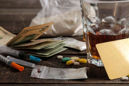 Various addictive drugs including alcohol, cigarettes, and drugs on a brown wooden table. Drug addiction conceptの写真素材