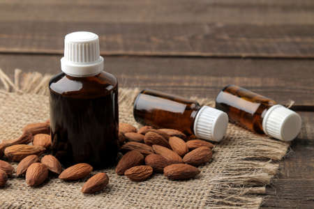 natural almond cosmetic oil in a glass bottle and fresh almond nuts close-up on a brown wooden table.の写真素材