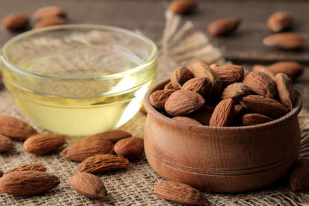 natural almond oil in a glass bottle and fresh almond nuts close-up on a brown wooden table.の写真素材