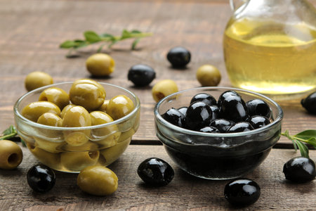 green and black olives with olive oil and leaves on a brown wooden table. close-up
