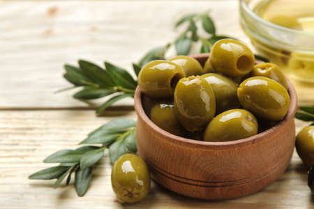 green olives with leaves in a wooden bowl with olive oil on a natural wooden table. close-upの写真素材