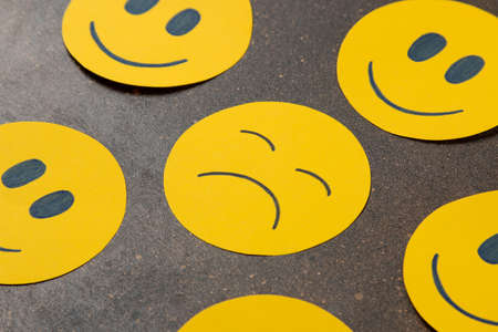 Depression concept. Psychological illness. sad smiley among funny smileys on a dark background.の写真素材