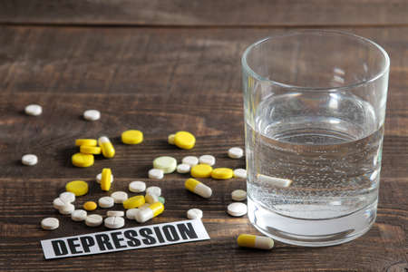 Depression concept. a glass of water, the inscription depression and pills on a wooden brown table.の写真素材