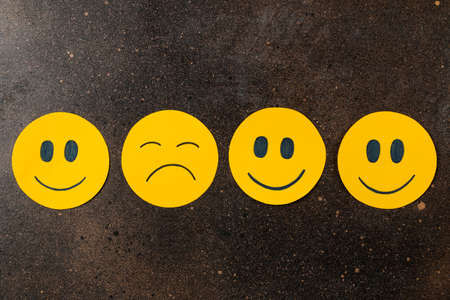 Depression concept. sad smiley among funny smileys on a dark background. top viewの写真素材