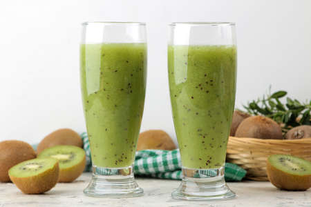 Kiwi smoothies in a glass next to fresh kiwi slices on a light marble table. fruit drink.の写真素材