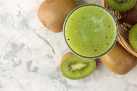 Kiwi smoothies in a glass next to fresh kiwi slices on a light marble table. fruit drink. top view. free spaceの写真素材