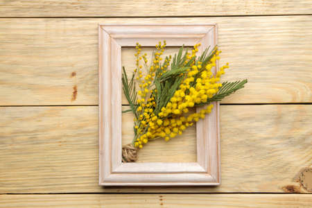 Beautiful bouquet of yellow mimosa flowers and a frame on a natural wooden table. top viewの写真素材