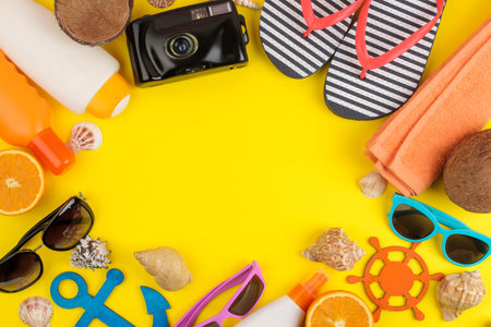 summer accessories with sun glasses, a hat, shells, flip flops, a camera on a bright yellow...