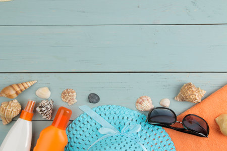 summer accessories. beach accessories. sunscreens, a hat, shells, and sunglasses on a blue wooden...