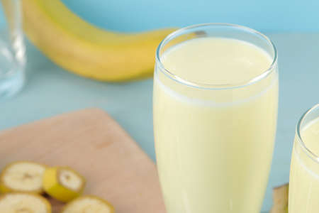 A glass with a banana milkshake and a fresh banana on a blue background. Making a milkshake.の写真素材