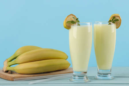 A glass with a banana milkshake and a fresh banana on a blue background. Making a milkshake.の写真素材