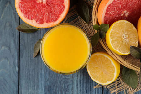 Citrus fruit. various citrus fruits with leaves of lemon, orange, grapefruit in a basket and orange juice on a blue wooden table. top viewの写真素材