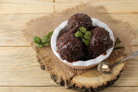 Chocolate ice cream with liquid chocolate and a mint leaf on a natural wooden background.