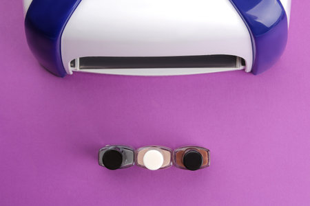 Manicure. UV lamp and nail polish on a trendy purple background. Manicure accessories and tools for...