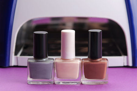 Manicure. UV lamp and nail polish on a trendy purple background. Manicure accessories and tools for...