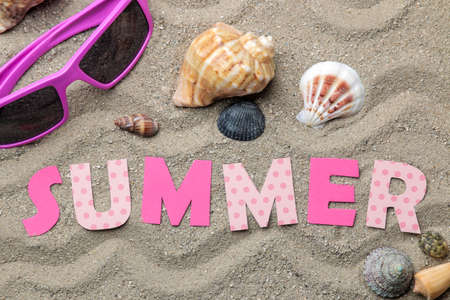Inscription summer from paper of multi-colored letters and seashells and summer accessories on the sea sand. Summer relaxation. vacation. top viewの写真素材