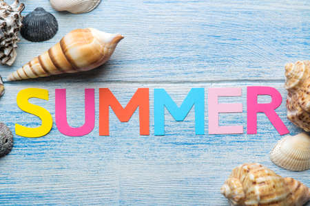 Inscription summer from paper of multi-colored letters and seashells and summer and sea accessories on a blue wooden table. Summer relaxation. vacation. top viewの写真素材
