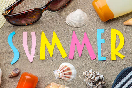 Inscription summer from paper of multi-colored letters and seashells and summer accessories on the sea sand. Summer relaxation. vacation. top viewの写真素材