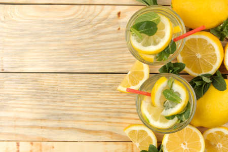 Homemade lemonade with mint and lemon in plastic glasses on a natural wooden background. Refreshing lemonade drink. top viewの写真素材