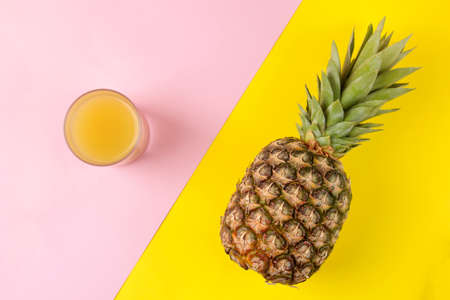 Large ripe fruit pineapple and pineapple juice on a bright yellow and pink background. summer. top view.の写真素材