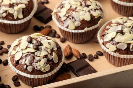 Delicious, sweet chocolate muffins, with almond petals in a wooden tray next to grains of coffee on a blue wooden table.の写真素材