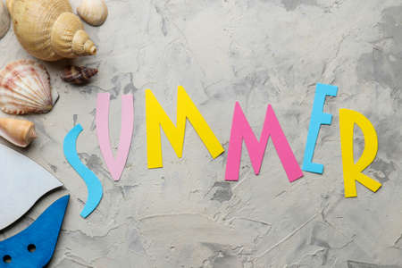 The word summer from paper with multicolored letters and sea accessories, shells on a light concrete background. summer. vacation. relaxation. top viewの写真素材