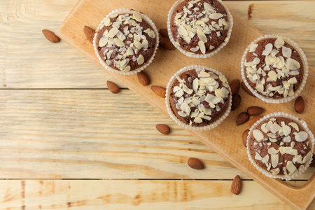 Delicious, sweet chocolate muffins, with almond petals next to almond nuts on a natural wooden...