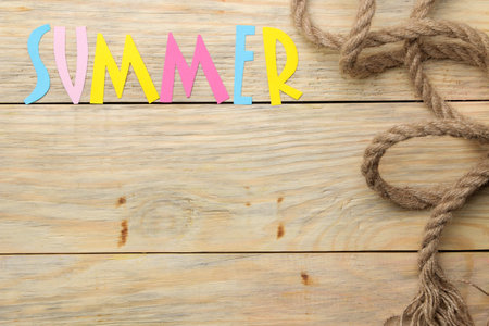 The word summer made of paper multicolored letters and sea rope on a natural wooden background....