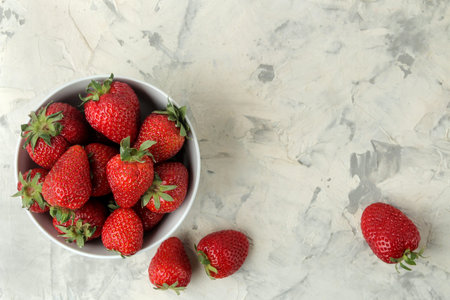 Ripe, delicious strawberries. Red strawberry in a ceramic bowl on a light concrete table. top view